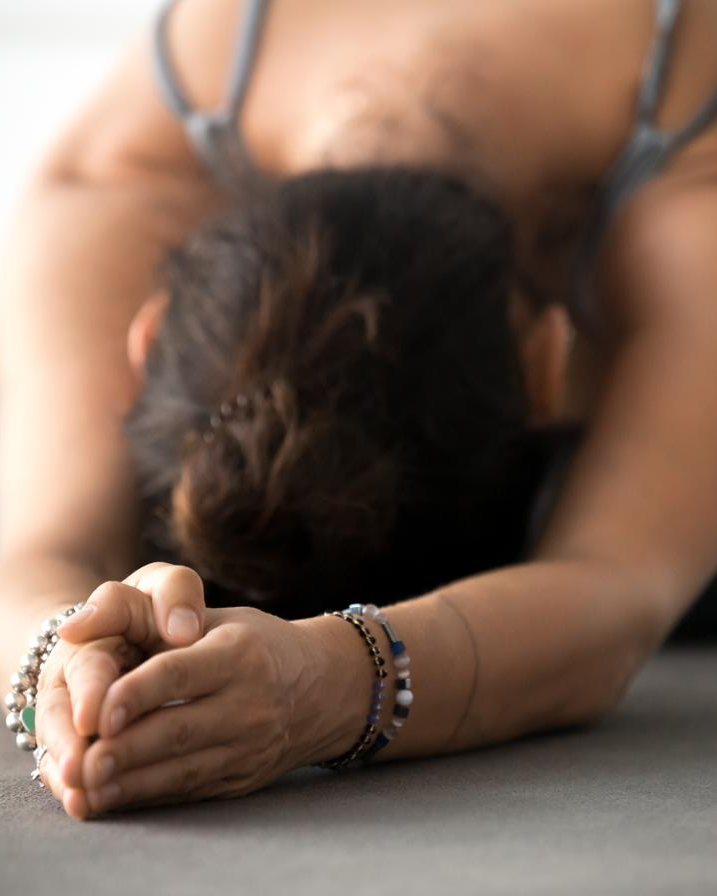A woman resting in a supported forward fold, forehead lowered to her hands