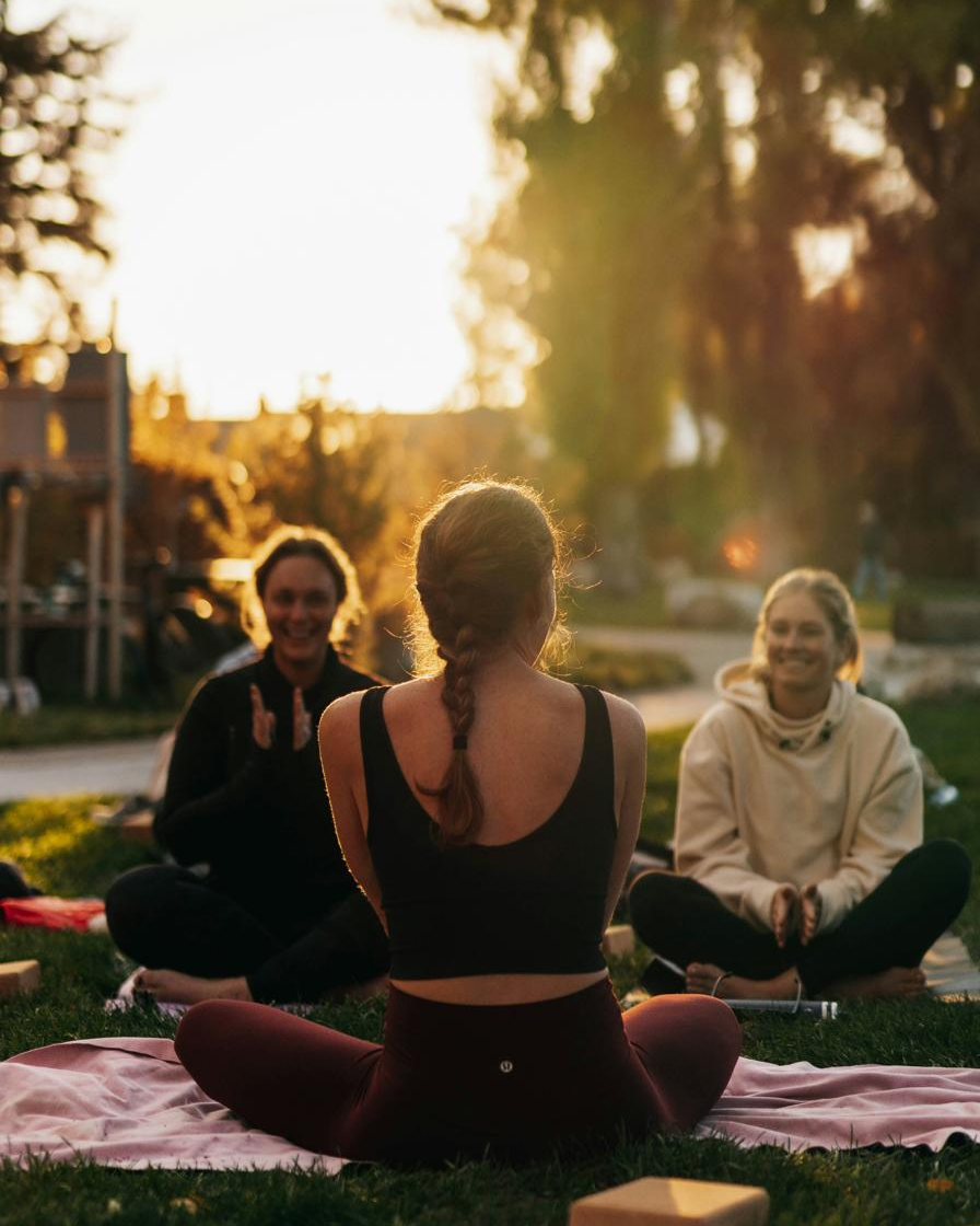A yin yoga instructor guiding two students in an outdoor session at golden hour