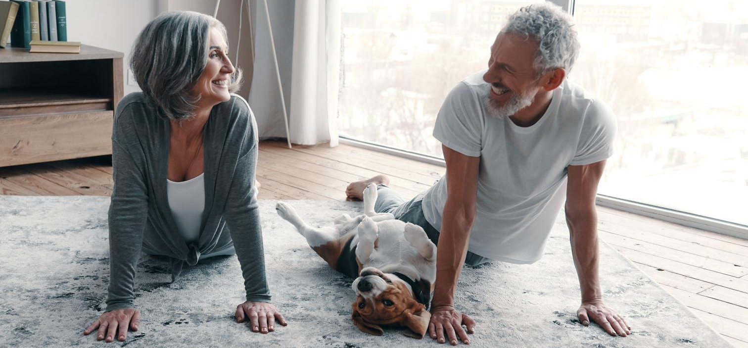 An older couple practicing yoga together at home with their dog